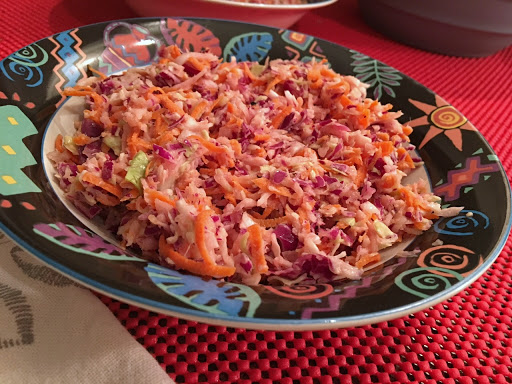 Coleslaw in a bowl sitting on a red table mat with white napkin.